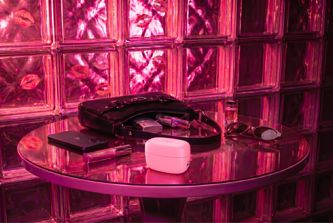Étui de recharge du Womanizer Snap posé sur une table avec un sac, un téléphone et des lunettes